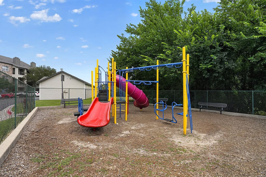 A playground with a red slide and a yellow and blue swing set.